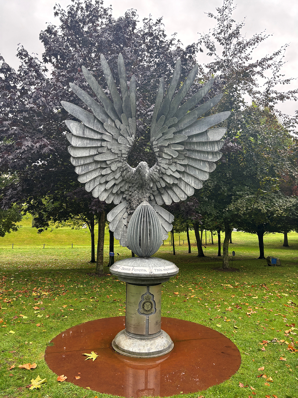 The Number 216 Squadron memorial, a pedestal depicting the official Squadron badge and etched representations of aircraft that the Squadron has been equipped with. Atop the pedestal is a representation of an eagle, its wings spread, such that they arch over the body and the wing tips almost meet over it's head.